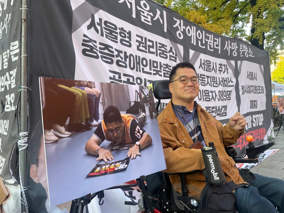 조재범 장애인자립생활센터 판 활동가가 자신의 포체투지 사진과 함께 포즈를 취하고 있다. 사진 전장연