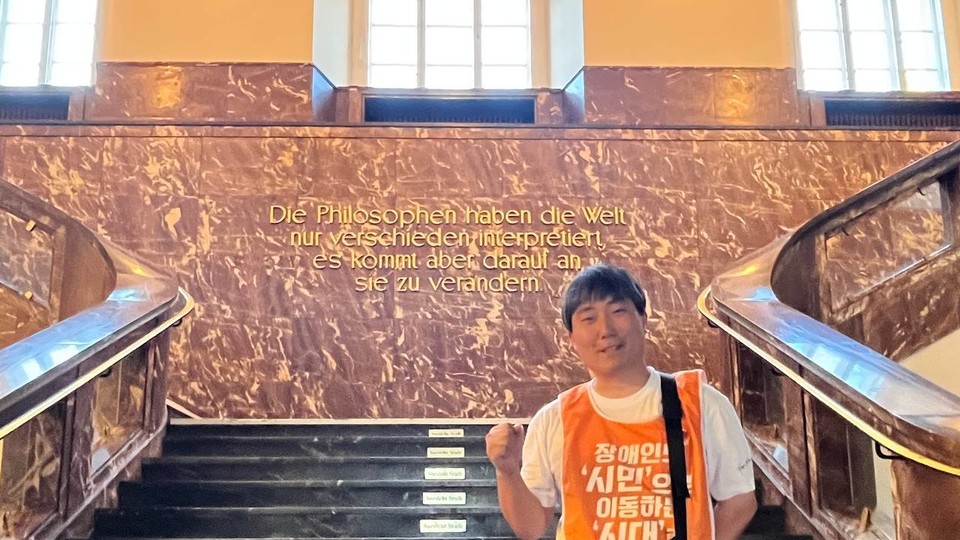 훔볼트 대학의 건물 벽에 마르크스의 글귀가 독일어로 쓰여 있다.  해당 글귀 앞에 이정한 활동가가 주먹을 쥐며 사진을 찍고 있다. 사진 이정한 활동가 제공