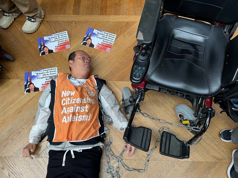 박상호 소장이 목과 휠체어에 쇠사슬을 두르고 루브르박물관 바닥에 누워있다. 사진 전장연 제공