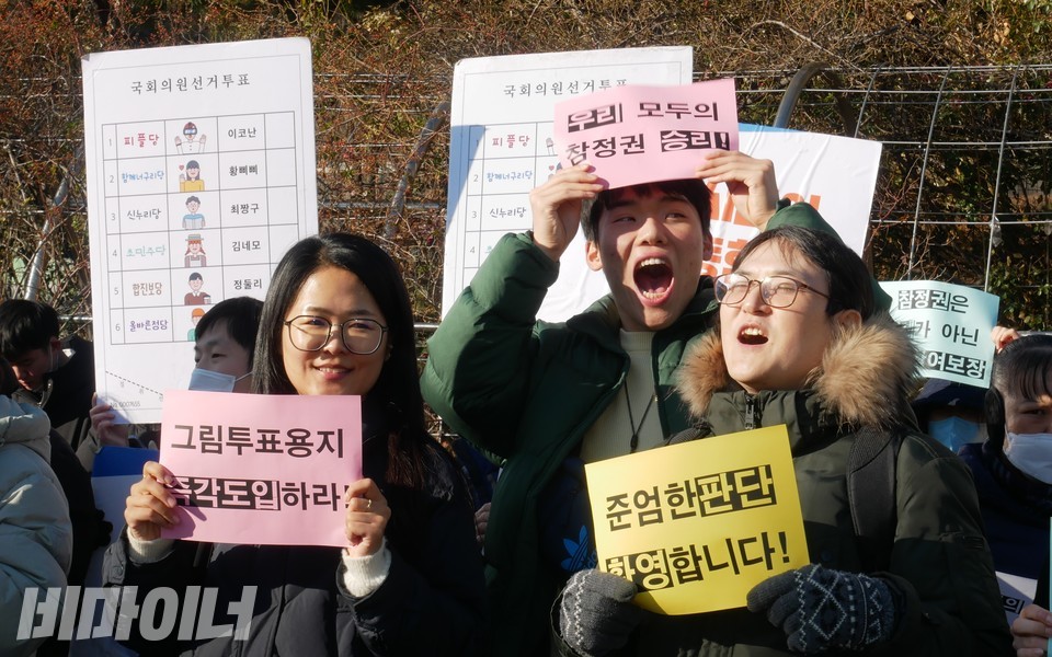 기자회견 참가자들이 미소를 짓고 있다. 김재왕 변호사는 “준엄한 판단 환영합니다”라고 적힌 피켓을 들고 있다. 사진 하민지