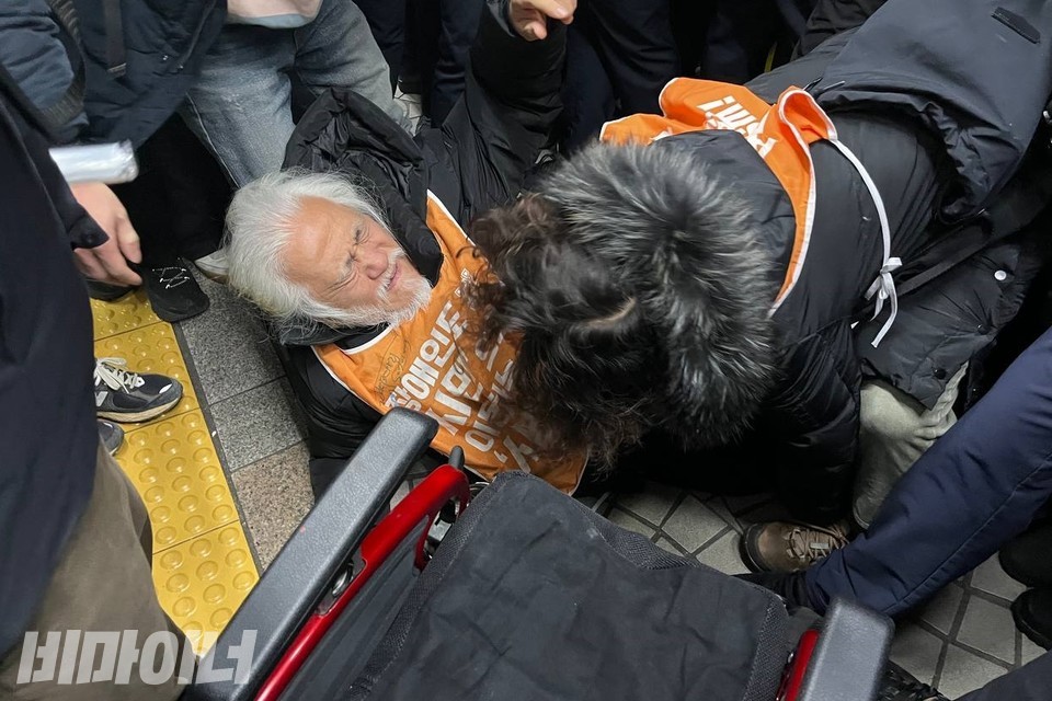 박경석 전장연 상임공동대표가 승강장으로 들어서자, 휠체어 발판을 방패 삼아 든 서울교통공사 보안관들과 경찰들이 그를 막아섰다. 그들과 대치하다 휠체어 아래로 넘어진 박경석 대표가 고통스러워하고 있다. 사진 김소영