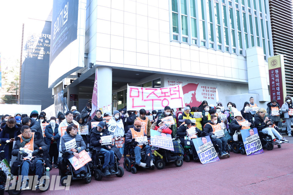 장애인들을 비롯한 시민들이 동덕여대 학생들과 연대하기 위해 동덕여대 공연예술센터로 행진을 마쳤다. 시민들이 “민주동덕”이라고 빨간색 글씨로 쓰인 흰 천을 들고 있다. 사진 김소영