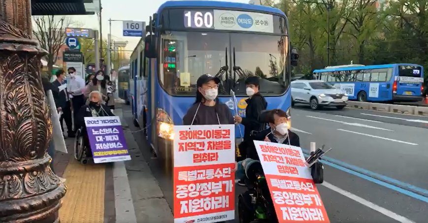 지난 2021년 4월 8일, 서울 종로구 혜화동 마로니에 공원 앞 버스정류장으로 들어오는 160번 버스를 막아선 전국장애인차별철폐연대 활동가들. 박경석 전장연 대표는 장애인 이동권 보장을 요구하며 버스 출입문과 자신의 휠체어를 쇠사슬로 단단히 묶은 채 15분간 기습 시위를 벌였다. 전장연 페이스북 영상 캡처