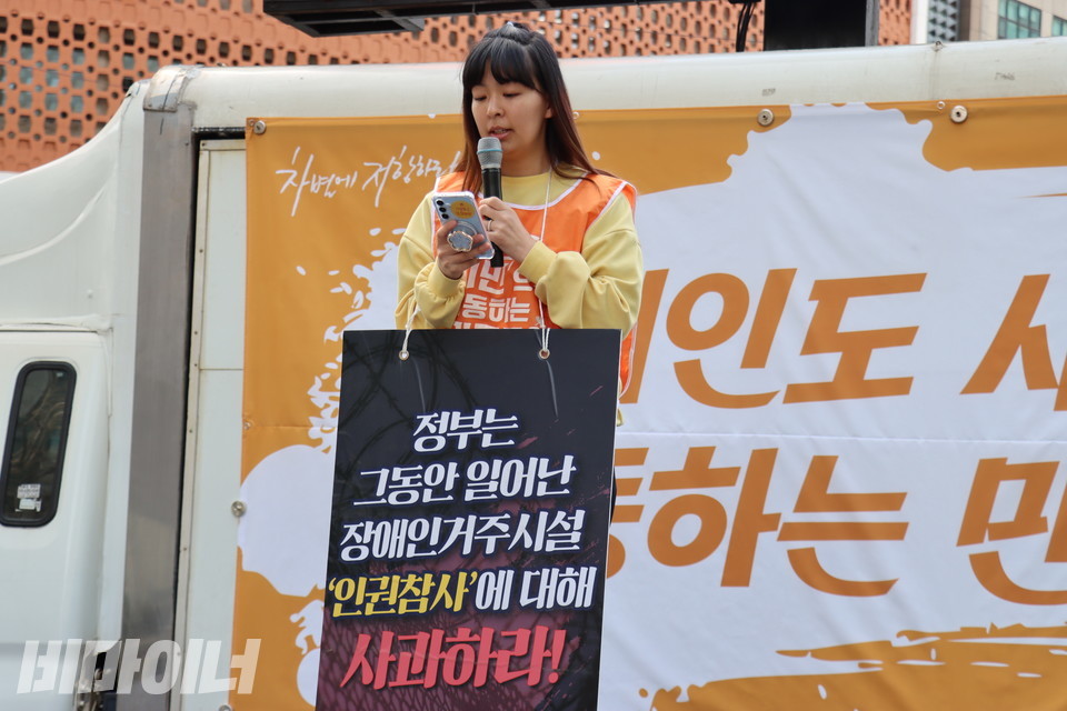 박초현 전국탈시설장애인연대 서울지부 공동대표가 발언하고 있다. 그의 목에는 “정부는 그동안 일어난 장애인거주시설 ‘인권참사’에 대해 사과하라!”라고 적힌 피켓이 걸려있다. 사진 김소영