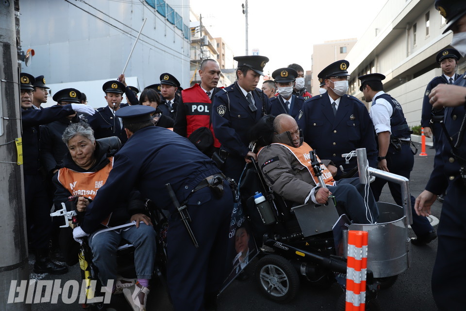 주일본대한민국대사관 앞에서 일본 경찰들이 문경희 대표의 동의 없이 그의 휠체어를 들어 올린 뒤 내려놓고 있다. 문 대표가 불편한 듯한 표정을 짓고 있다. 사진 김소영