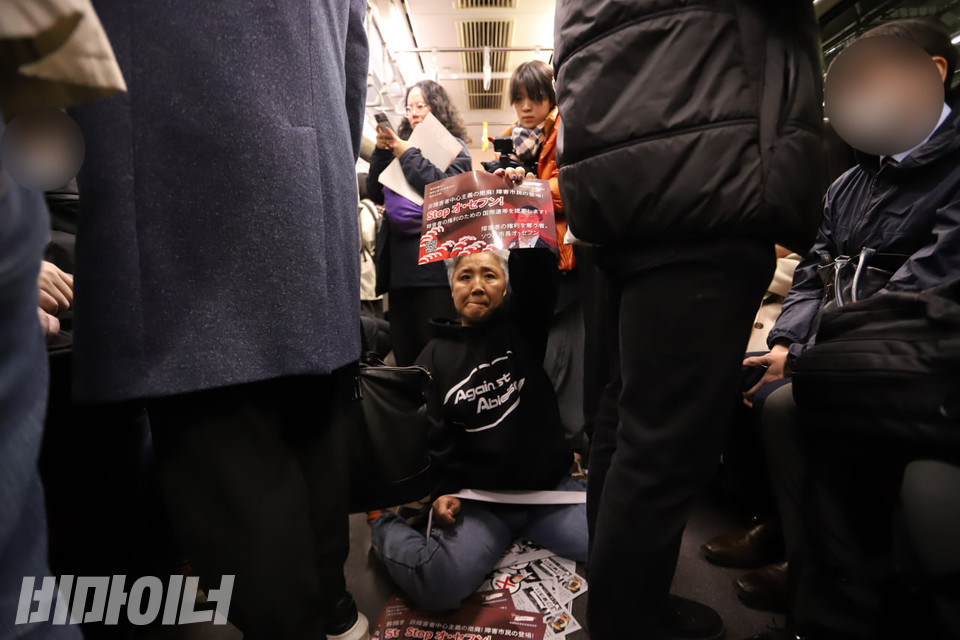 문경희 세종장애인차별철폐연대 상임공동대표가 일본 지하철에서 포체투지를 하고 있다. 그는 일본어로 쓰인 권리스티커를 높이 들고 있다. 사진 김소영