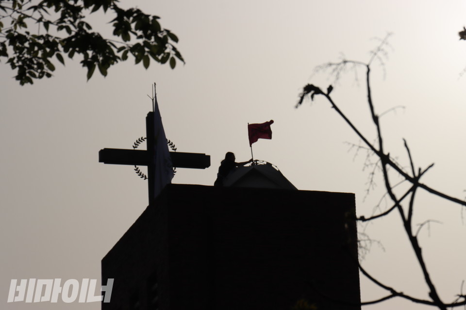 전국장애인차별철폐연대와 전국탈시설장애인연대 활동가 3명이 18일 오후 4시께 서울시 종로구 혜화동성당 종탑 꼭대기에 올랐다. 한 활동가가 종탑에서 깃발을 올리고 있다. 사진 김소영