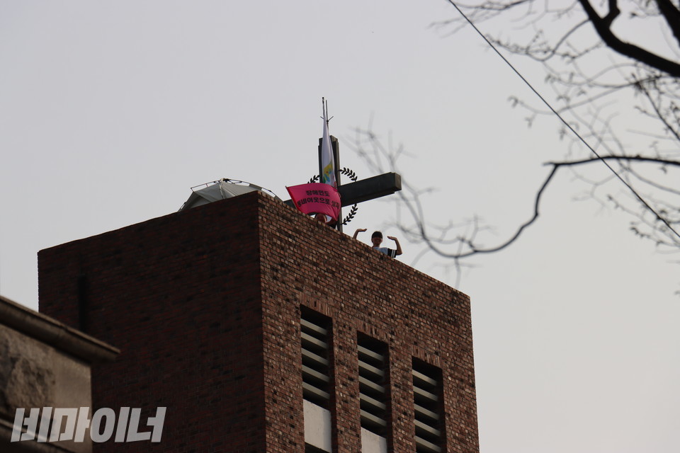 종탑에 올라가 있는 민푸름 활동가와 박초현 활동가. 민푸름 활동가가 “장애인도 동네 이웃으로 살자”라고 적힌 깃발을 들고 있다. 사진 김소영