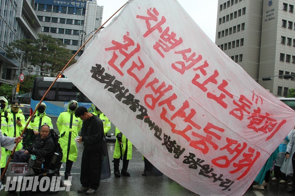 커다란 현수막에 “차별생산노동 철폐, 권리생산노동 쟁취, 권리중심 중증장애인 맞춤형 공공일자리”라고 적혀 있다. 현수막 앞에 이규식 서울장차연 상임대표가 있다. 사진 하민지