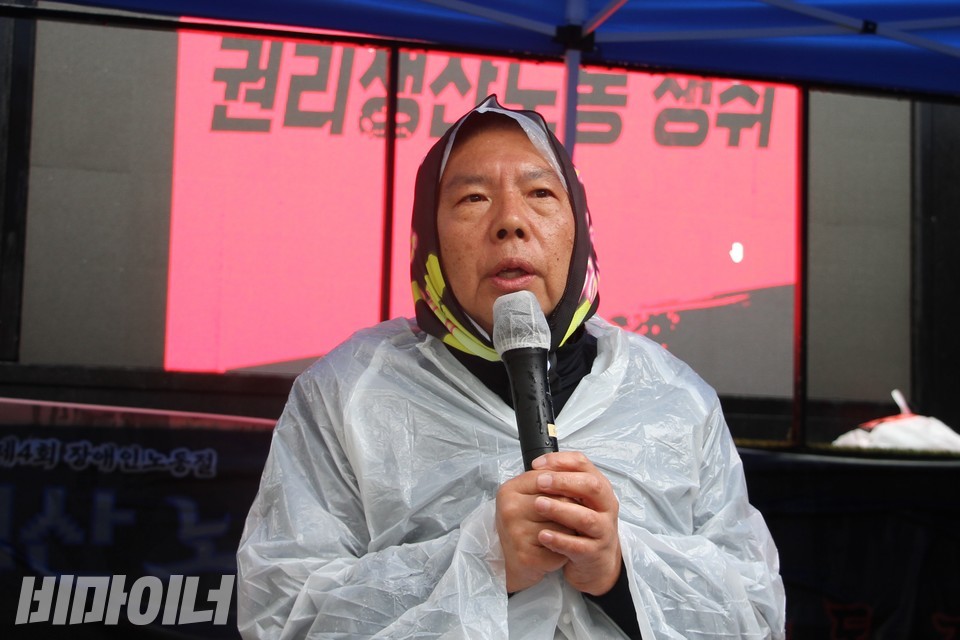 권달주 전장연 상임공동대표가 발언 중이다. 그의 뒤로 “권리생산노동 쟁취”라고 적힌 화면이 보인다. 사진 하민지
