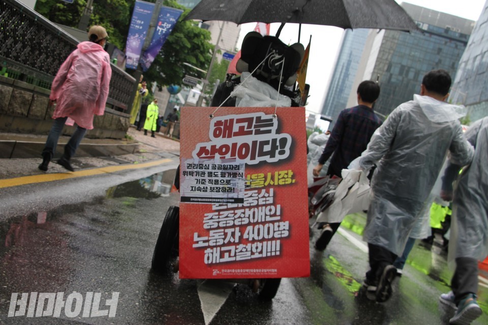 “해고는 살인이다”라고 적힌 피켓을 휠체어에 걸고 행진하는 사람. 사진 하민지
