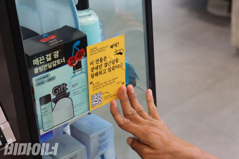 장애인 활동가가 올리브영 점포 진열대 벽면에 “이 건물은 장애인 접근권을 침해하고 있습니다”라고 적힌 ‘권리스티커’를 붙이고 있다. 사진 김소영