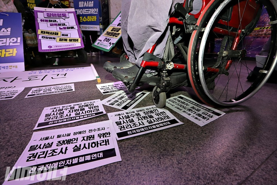 박경석 전장연 대표의 발과 휠체어 바퀴가 보인다. 그 아래 종이 피켓이 놓여 있다. 피켓에는 “서울시 탈시설 장애인 전수조사 탈시설 장애인 지원 위한 권리조사 실시하라”라고 적혀 있다. 사진 하민지