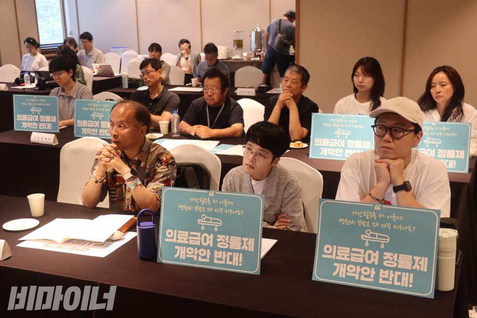 공개 집담회 참석자들이 집담회를 지켜보고 있다. 그들의 앞에는 “의료급여 정률제 개악안 반대!”라고 적힌 하늘색 피켓이 놓여있다. 사진 김소영