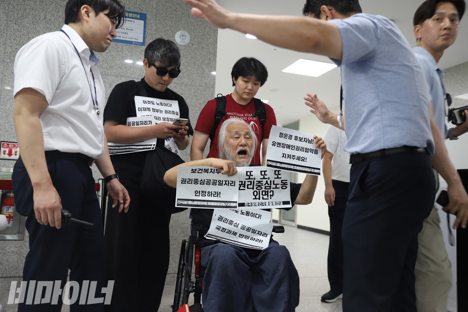 국정기획위원회에서 긴급행동을 벌이는 박경석 전국장애인차별철폐연대 상임공동대표가 종이 피켓을 들고 권리중심공공일자리 국정과제 반영을 요구하고 있다. 그 앞을 국정위 관계자가 막고 있다. 사진 김소영