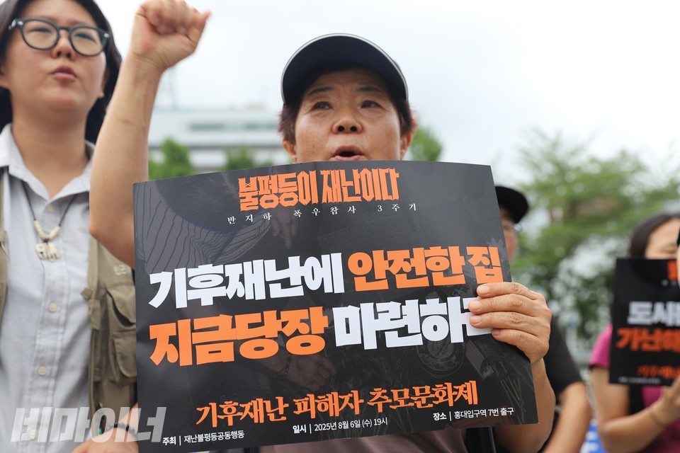 한 기자회견 참가자가 주먹 쥔 손을 높이 들며 구호를 외치고 있다. 그의 다른 손에는 “불평등이 재난이다”, “기후재난에 안전한 집 지금 당장 마련하라”라고 적힌 피켓이 들려있다. 사진 김소영