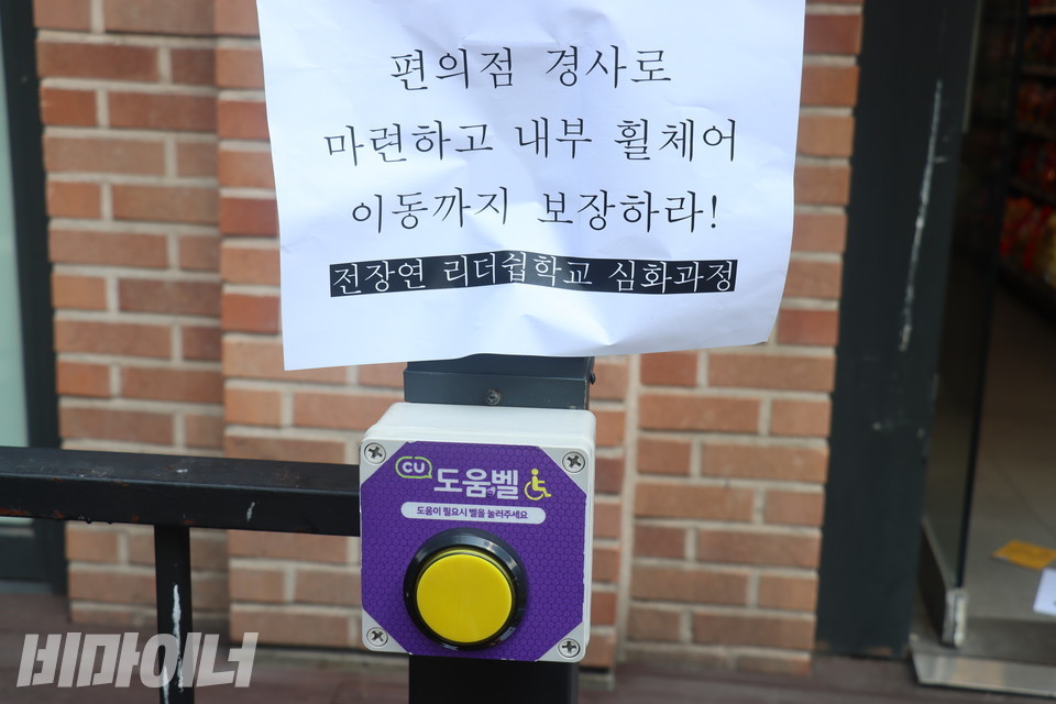 편의점 외부 난간에 설치된 도움벨. 그 위에 “편의점 경사로 마련하고 내부 휠체어 이동까지 보장하라!”고 적힌 종이가 붙어있다. 사진 김소영