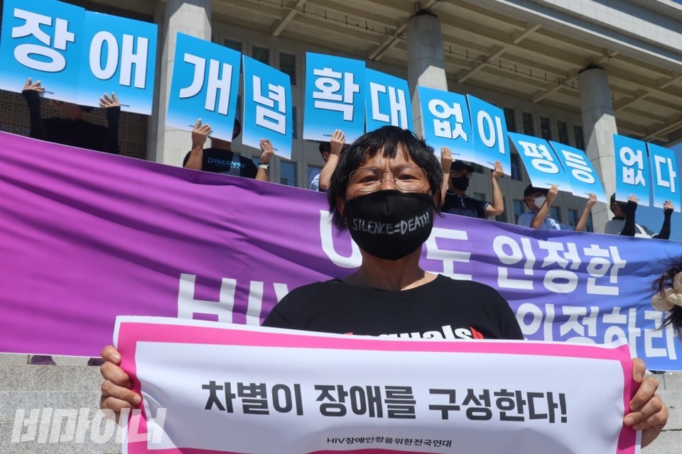 HIV장애인정을위한전국연대 활동가가 "차별이 장애를 구성한다" 손피켓을 들고 국회 앞에 서있다. 사진 이재민