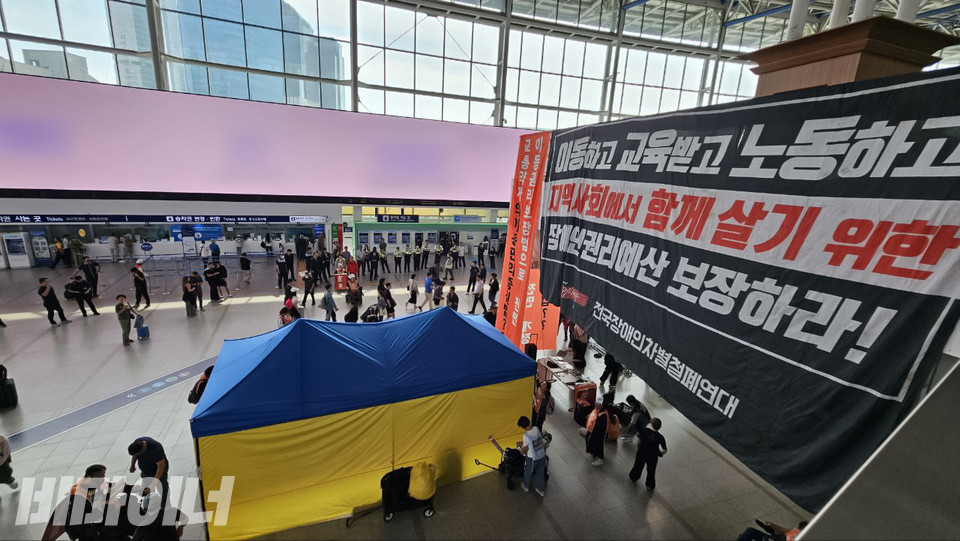 서울역 대합실에 설치된 장애인이동권 보장 천막 농성장 모습. 농성장 윗쪽 벽에 '이동하고 교육받고 노동하고 지역사회에서 함께 살기 위한 장애인권리예산 보장하라'라고 적힌 대형현수막이 걸여 있다. 사진 전장연