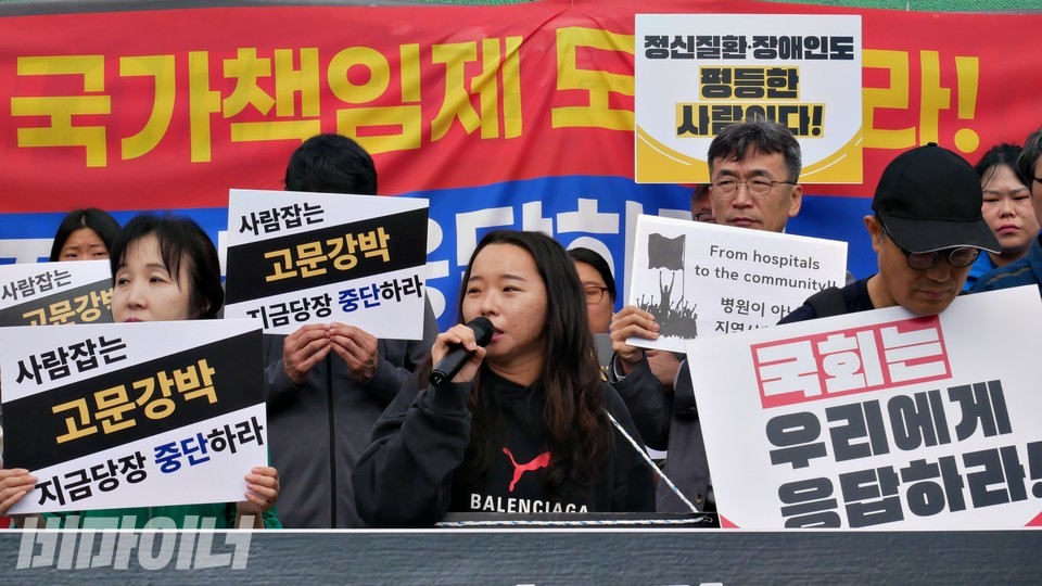 위은솔 한국정신장애인자립생활센터 센터장이 발언 중이다. “사람 잡는 고문강박 지금 당장 중단하라”, “국회는 우리에게 응답하라”, “정신질환·장애인도 평등한 사람이다”라고 적힌 피켓들이 있다. 사진 하민지
