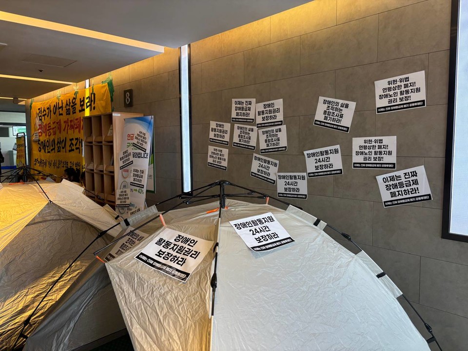 국민연금공단 강동하남지사 로비에 원터치텐트가 설치되어 있고 벽에 스티커가 붙여져 있다. 사진 서울장애인차별철폐연대