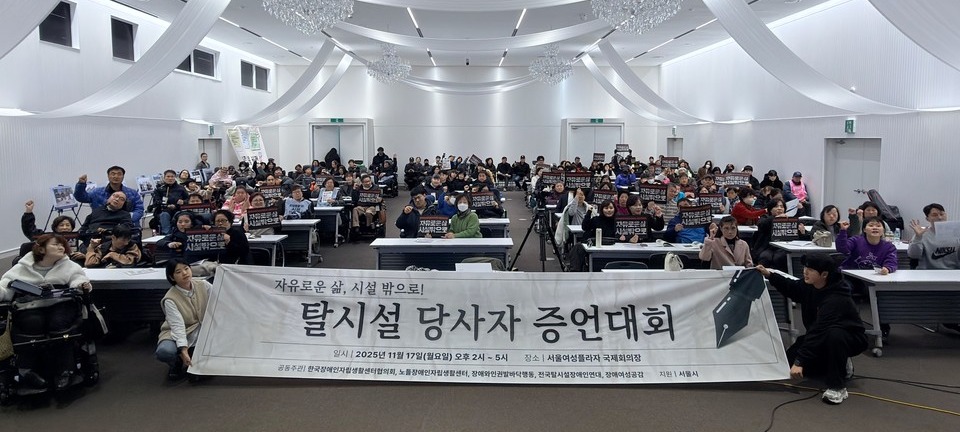   지난 17일 오후 2시에 열린 ‘2025년 탈시설 당사자 증언대회’ 현장. 참석자들이 “자유로운 삶, 시설 밖으로”라고 적힌 피켓을 들고 손을 번쩍 들고 있다. 사진 한국장애인자립생활센터협의회