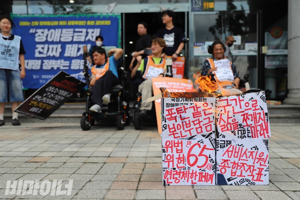 '현행 활동지원서비스 제도'라고 적힌 상자를 불태우는 퍼포먼스가 진행되고 있다. 사진 하민지