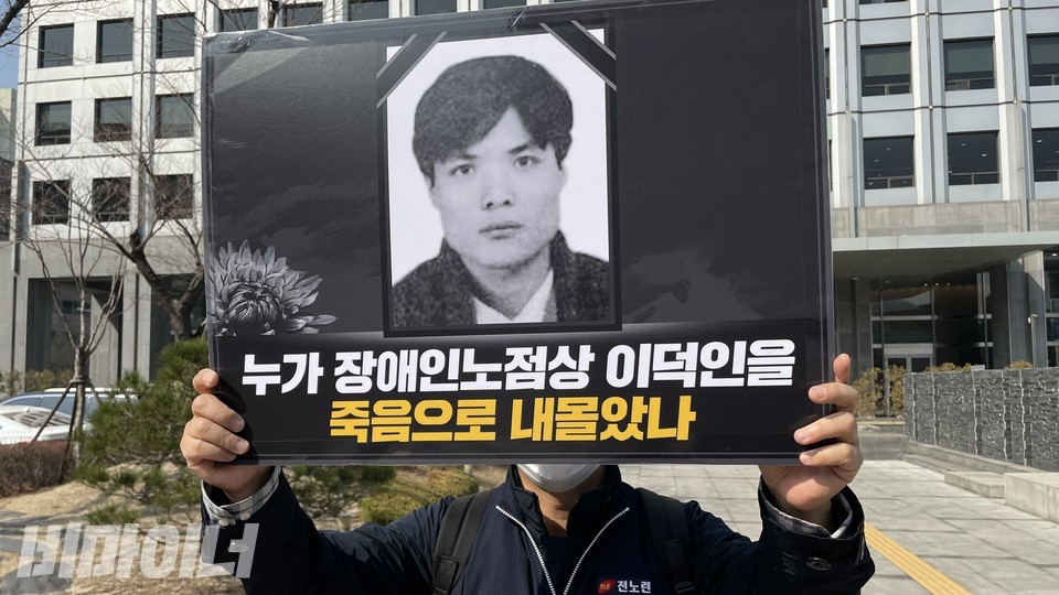 한 활동가가 '누가 장애인 노점상 이덕인을 죽음으로 내몰았나'라고 적혀있는 피켓을 들고 기자회견에 참여했다. 피켓에는 이덕인 열사의 영정사진이 있다. 사진 하민지