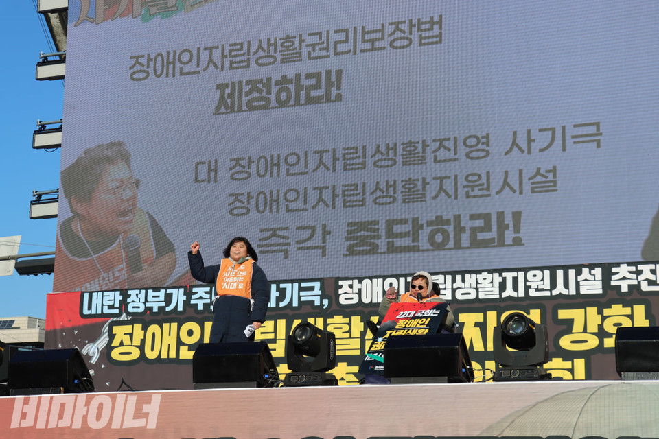 정다운 한자협 사무총장(왼쪽)과 이형숙 한자협 회장(오른쪽)이 구호를 외치고 있다. 그들의 뒤에 있는 LED 화면에 “장애인자립생활권리보장법 제정하라!”, “대 장애인자립생활진영 사기극 장애인자립생활지원시설 즉각 중단하라!”라고 적혀있다. 사진 김소영