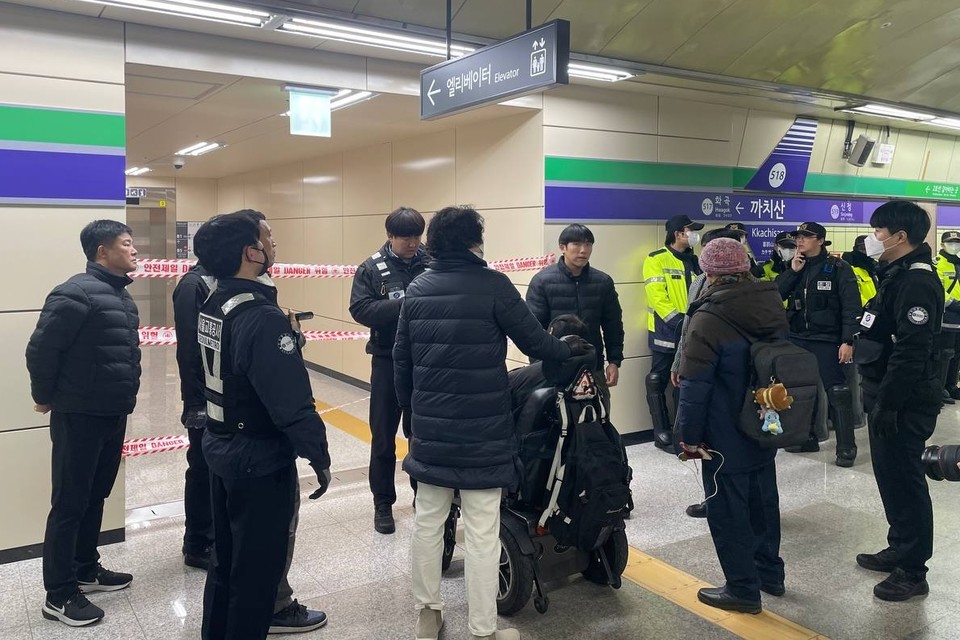 엘리베이터 앞이 테이프로 봉쇄돼있고 그 주변을 서울교통공사 보안관과 경찰이 둘러싸고 있다. 그들 앞에 휠체어 이용 장애인이 이동하지 못한 채 막혀있다. 사진 전장연