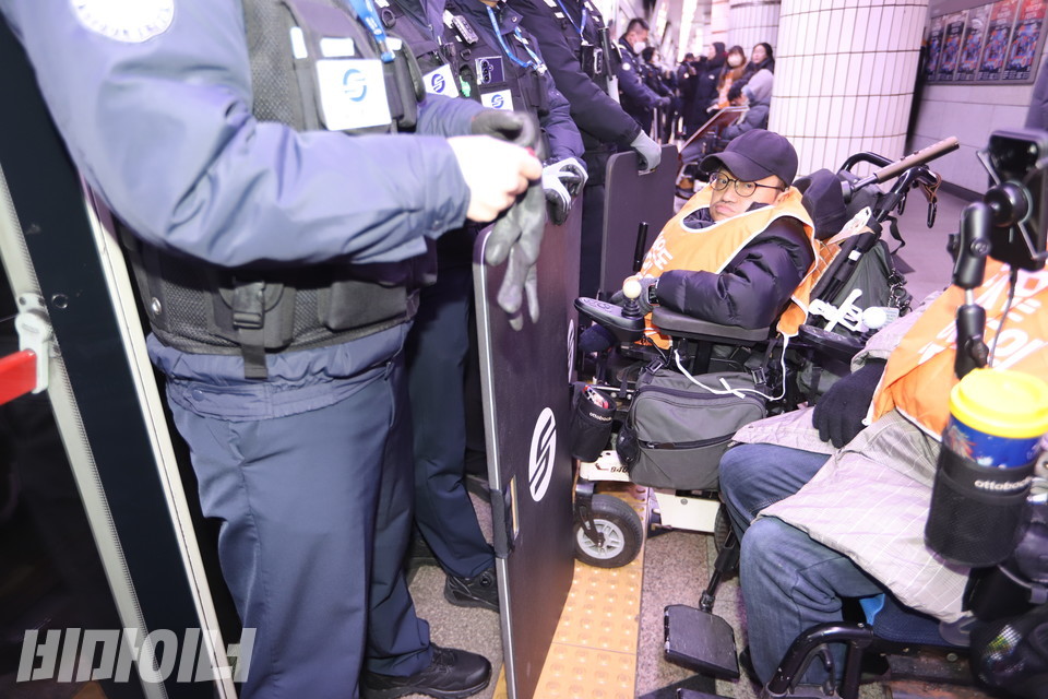 지하철 문 앞에서 방패를 든 채 가로막고 있는 공사 보안관들. 그 앞에 휠체어 이용 장애인이 앞으로 이동하지 못하고 있다. 사진 김소영