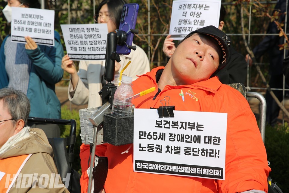 기자회견에 참석한 박지호 탈시설장애인당당 서울시장 노동권 후보. 그의 휠체어에 “보건복지부는 만 65세 장애인에 대한 노동권 차별 중단하라!”라고 적힌 종이가 붙어 있다. 사진 김소영