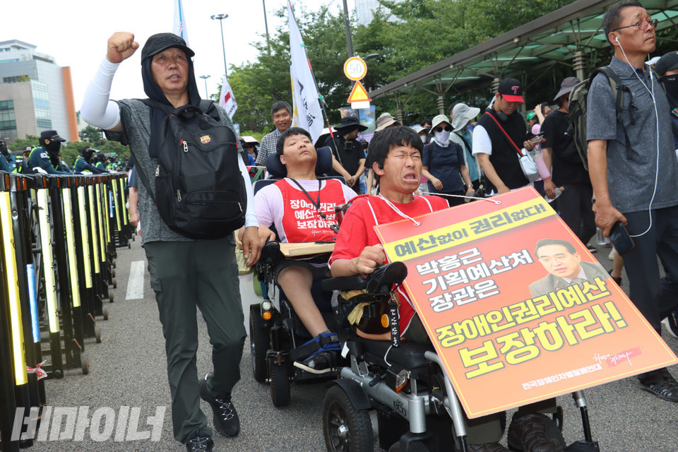전동행진 참가자들이 구호를 외치고 있다. 휠체어 이용 장애인 활동가의 목에는 “예산 없이 권리 없다. 박홍근 기획예산처 장관은 장애인권리예산 보장하라!”라고 적힌 피켓이 걸려있다. 사진 김소영