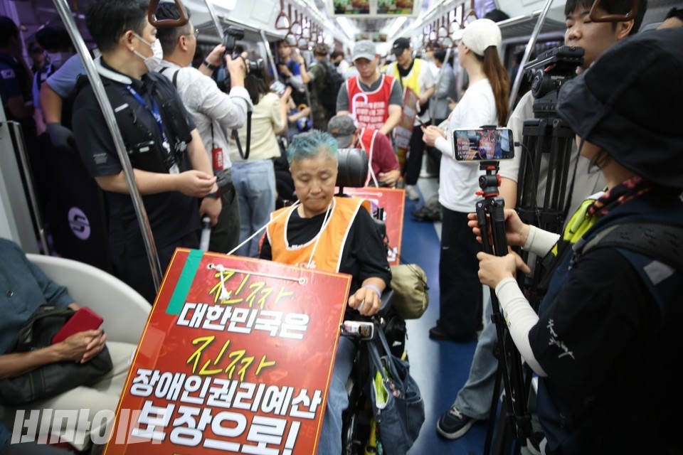 지하철에 탑승한 장애인 활동가. 목에는 "진짜 대한민국은 진짜 장애인권리예산 보장으로!"가 적혀있다. 사진 이재민
