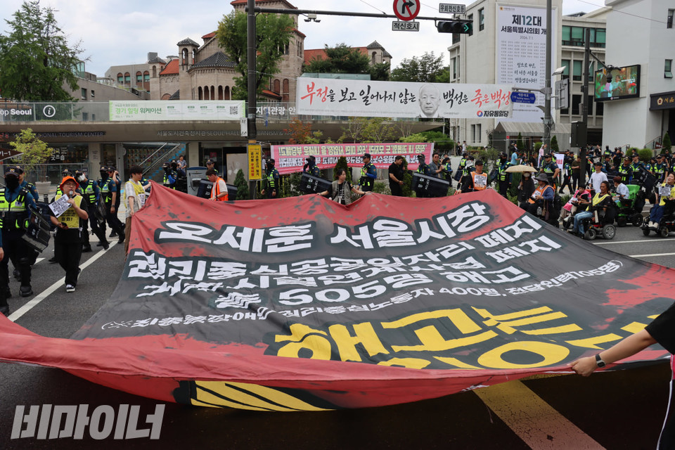 7일 오후 2시에 진행된 ‘서울시의회 권리중심공공일자리 제도화 촉구 총력집중 결의대회’ 직후 진행된 행진 현장. 참가자들이 “오세훈 서울시장 권리중심공공일자리 폐지, 거주시설 연계사업 폐지 총 505명 해고, 해고는 살인이다!”라고 적힌 대형 현수막을 들고 있다. 사진 김소영