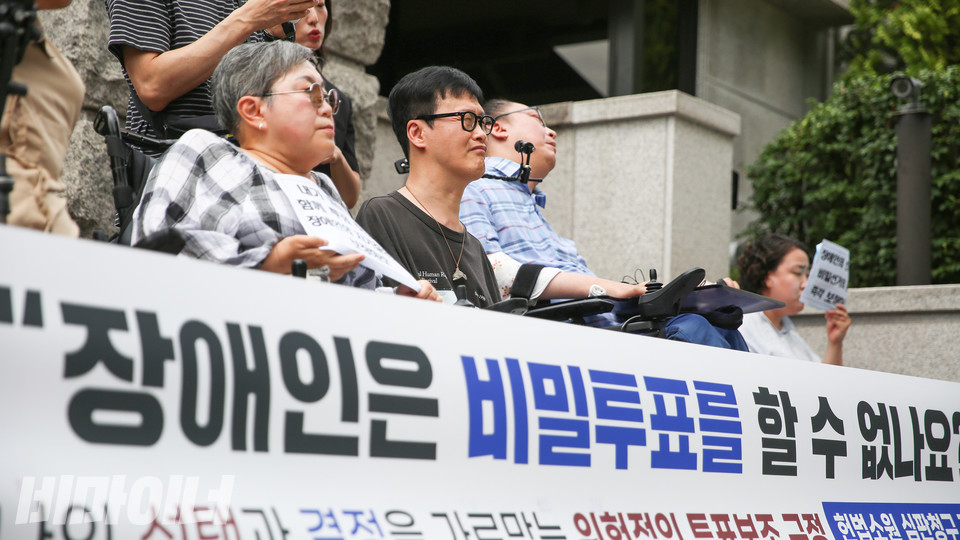 박김영희 대표와 김형호 씨가 발언을 듣고 있다. 두 사람 앞으로 현수막에 적힌 “장애인은 비밀투표를 할 수 없나요?”라는 글씨가 크게 보인다. 사진 장호경