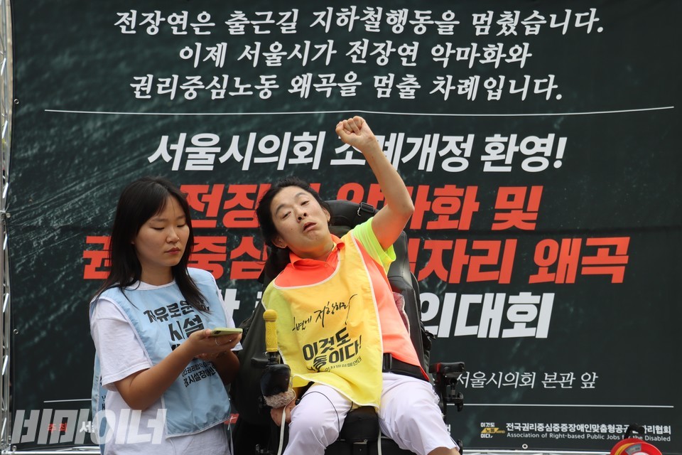 조상지 서울탈시설장애인당 대표가 AAC(보완대체의사소통) 기기를 통해 발언하고 있다. 왼손을 주먹 쥔 채 높이 들어 올리고 있다. 사진 김소영