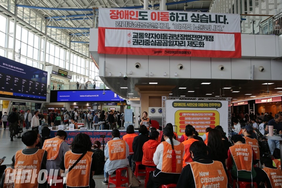 서울역에 설치된 전국장애인차별철폐연대 추석 농성장. 1층의 긴 테이블에 시민들에게 나눠 줄 유인물과 교통약자이동권보장법 제정을 위한 1만인 서명운동 서명지가 놓여있다. 농성장 바로 위 난간에는 "장애인도 이동하고 싶습니다. 권리중심일자리, '이것도 노동입니다'"가 적힌 현수막이 걸려 있다. 사진 이재민
