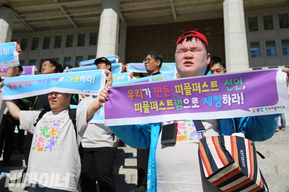 국회 본청 앞에서 “우리가 만든 피플퍼스트 선언, 피플퍼스트법으로 제정하라!”라고 적힌 손피켓을 들고 있는 한국피플퍼스트 활동가. 사진 김소영